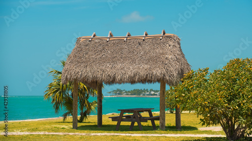 Fototapeta Naklejka Na Ścianę i Meble -  Exotic Tropical Shelter or bungalow on Ocean beach. Picnic place or area with thatched roof and wooden table. Sun protection. Summer vacations in Key West Florida. Palm Tree. Good for travel agency
