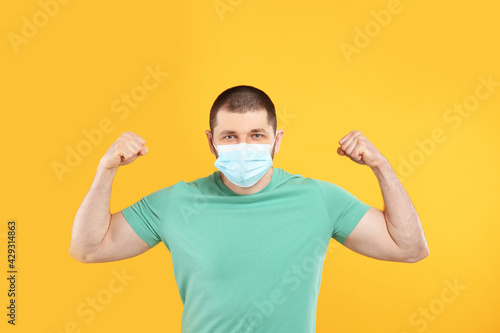Man with protective mask showing muscles on yellow background. Strong immunity concept