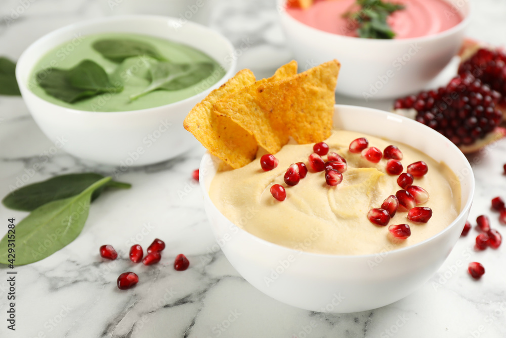 Bowl of delicious classic hummus with tortilla chips and pomegranate seeds on white marble table