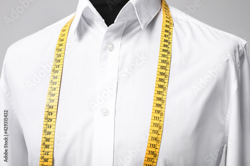 White shirt with tailor's measuring tape on mannequin against grey background, closeup