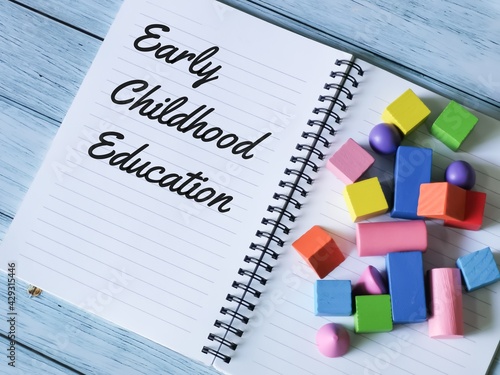 Phrase early childhood education written on notebook with a bunch colorful wooden cubes.