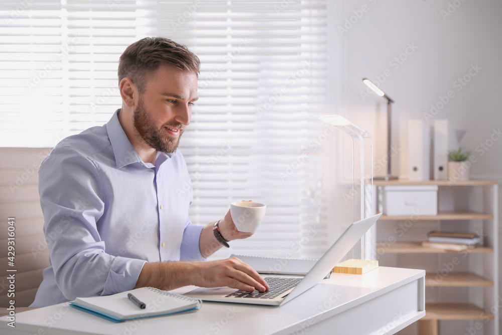Young man with coffee working on laptop at table in office Young man with coffee working on laptop at table in office