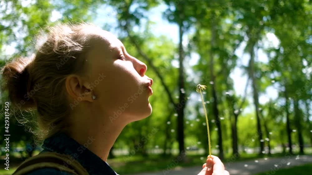 Woman blowing on white dandelion in summer park