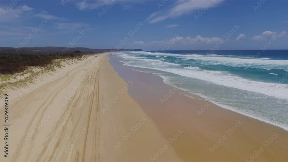 Smooth and slow descending aerial drone shot looking North over the dunes, tire tracks and bushland, down a deserted Main Beach, on North Stradbroke Island in Sunny Queensland, Australia Smooth and slow descending aerial drone shot looking North over the dunes, tire tracks and bushland, down a deserted Main Beach, on North Stradbroke Island in Sunny Queensland, Australia