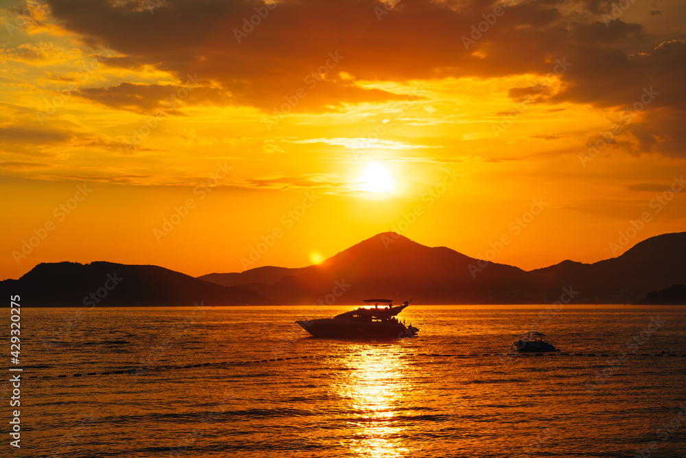 White motor yacht sails on the sea against the background of mountains at sunset