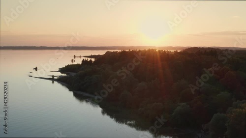 Lake Chiemsee in Bavaria with the Alp mountains during sunset from above, coast near village Chieming, during summer, flying forwards
 photo