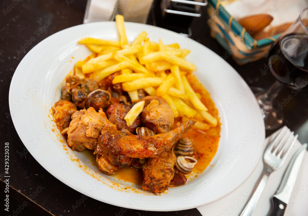 Appetizing stewed rabbit pieces with escargots served with vegetable garnish of French fries