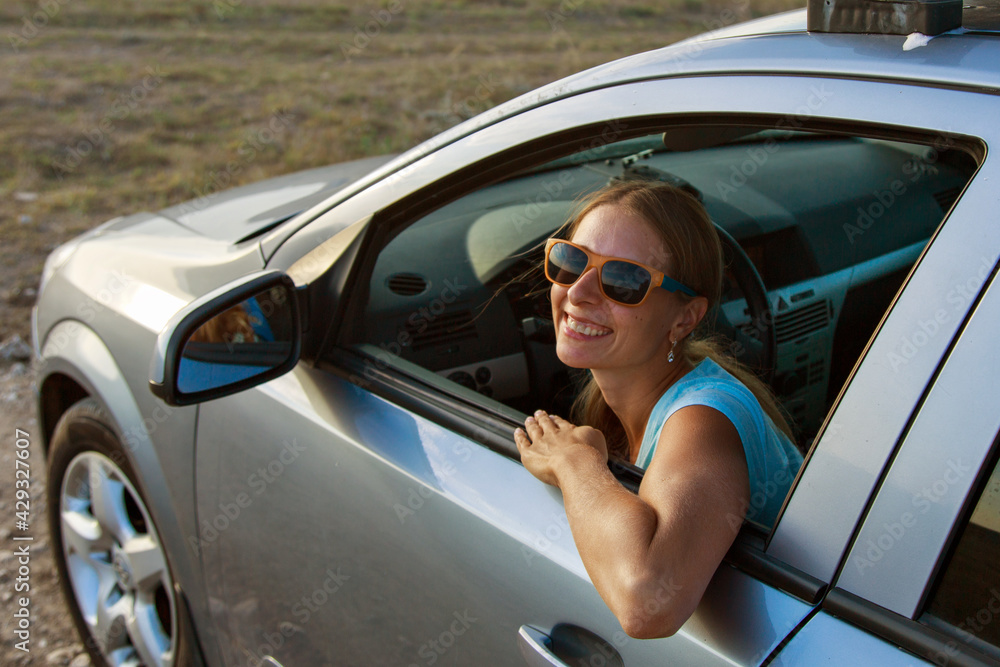 Naklejka premium travel by car. Happy girl with glasses looks out of the car