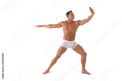Muscular shirtless man in yoga pose taking selfie on smartphone
