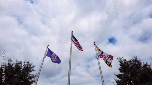 Flags of the USA, State of Maryland, and Talbot County, MD are waving on side by side flag posts on a cloudy day. photo