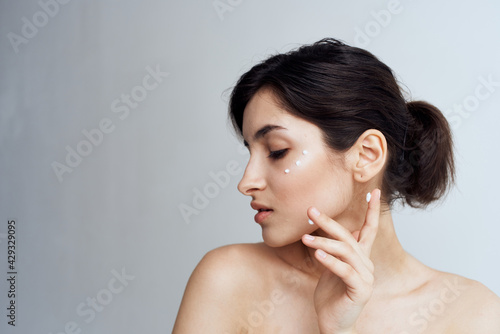Pretty brunette naked shoulders facial skin care cream close-up