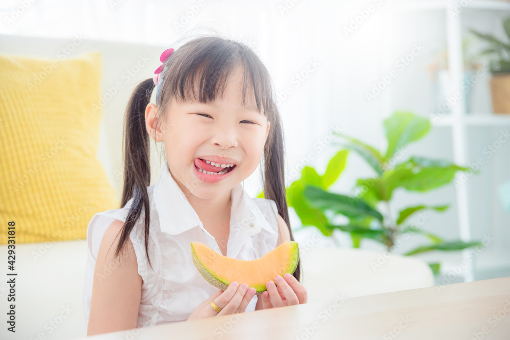 Pretty little asian girl eating melon at home. Healthy food and kid concept. Pretty little asian girl eating melon at home. Healthy food and kid concept.