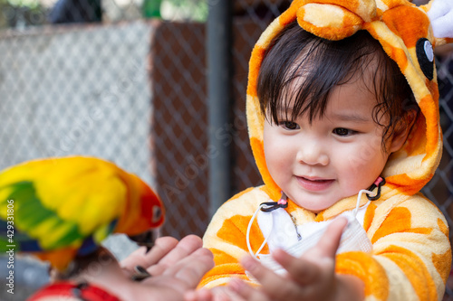 A cute Asian girl wearing a giraffe costume in a new normal state with a face mask, Go on a trip in the zoo, feed the Parrot in the large cage.