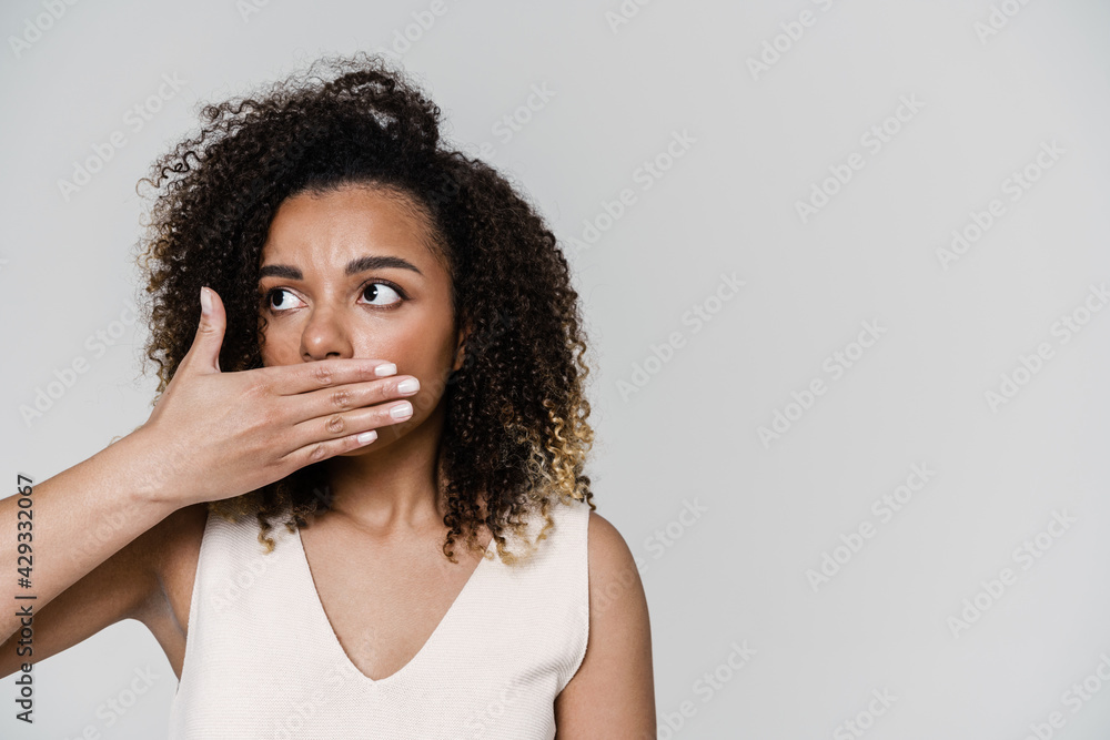 The portrait of a curly-haired woman looking to the side and covering her mouth with the hand in the studio The portrait of a curly-haired woman looking to the side and covering her mouth with the hand in the studio