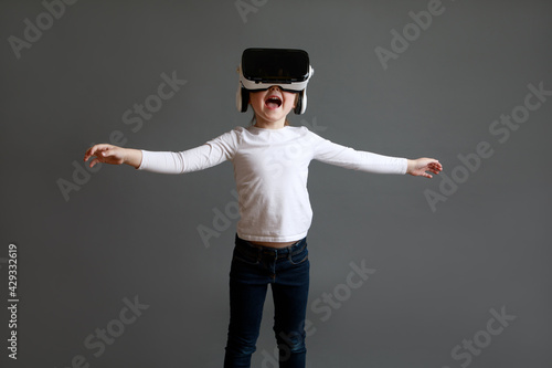 Fascinated female child in white long sleeve shirt wearing virtual reality glasses over grey background