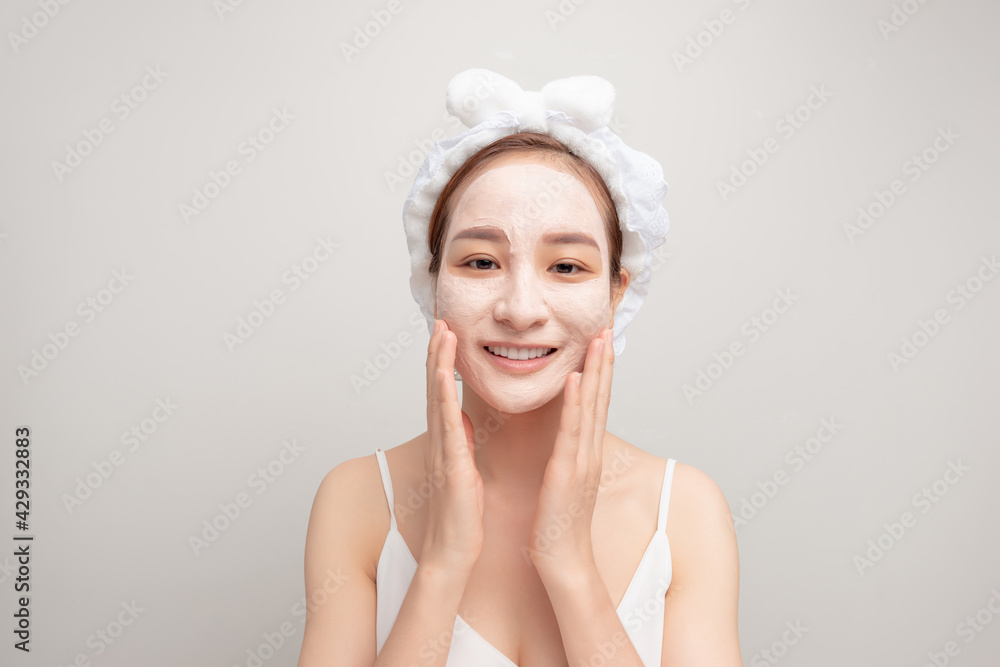 Portrait of confident lady in bathrobe and towel on head with joy while touching her face with clay mask while using anti-aging procedures Portrait of confident lady in bathrobe and towel on head with joy while touching her face with clay mask while using anti-aging procedures