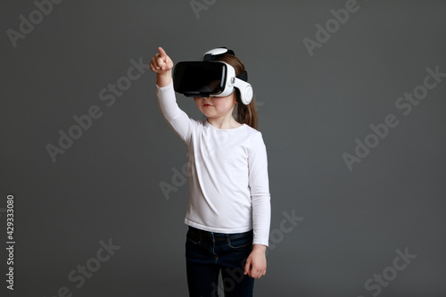 Little girl experiencing virtual reality eyeglassses in white long sleeve shirt over grey background