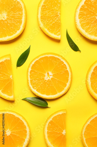 Slices of fresh oranges with green leaves on color background