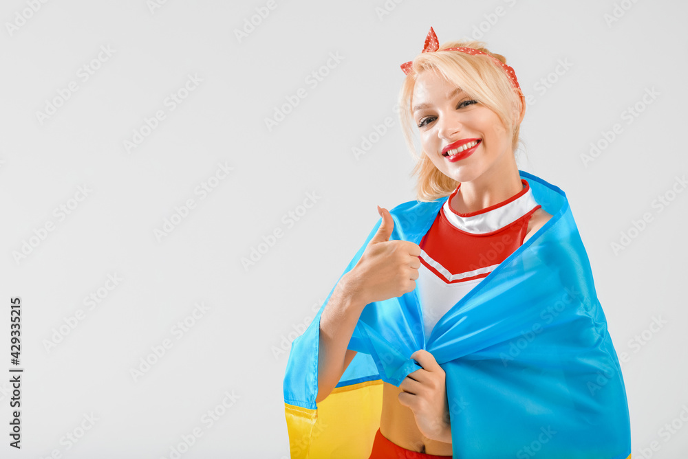 Beautiful cheerleader with flag of Ukraine on light background Beautiful cheerleader with flag of Ukraine on light background
