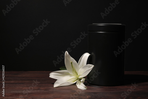 Mortuary urn with lily flower on table against dark background