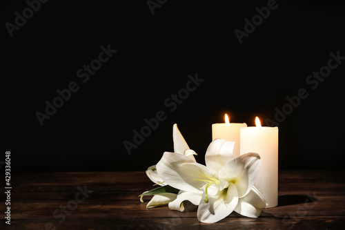 Foto Candles with lily flowers on table against dark background