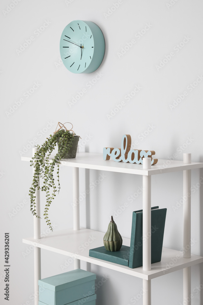 Shelf unit with clock near light wall in room - obrazy, fototapety, plakaty 