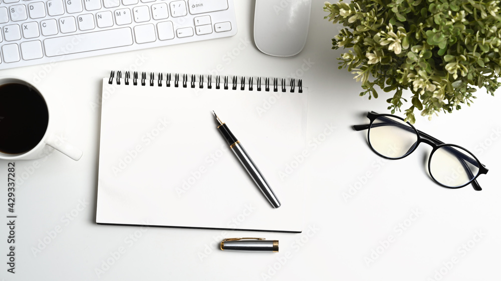 Top view of white office desk with empty notebook, glasses, house plant, coffee cup and pen. Top view of white office desk with empty notebook, glasses, house plant, coffee cup and pen.