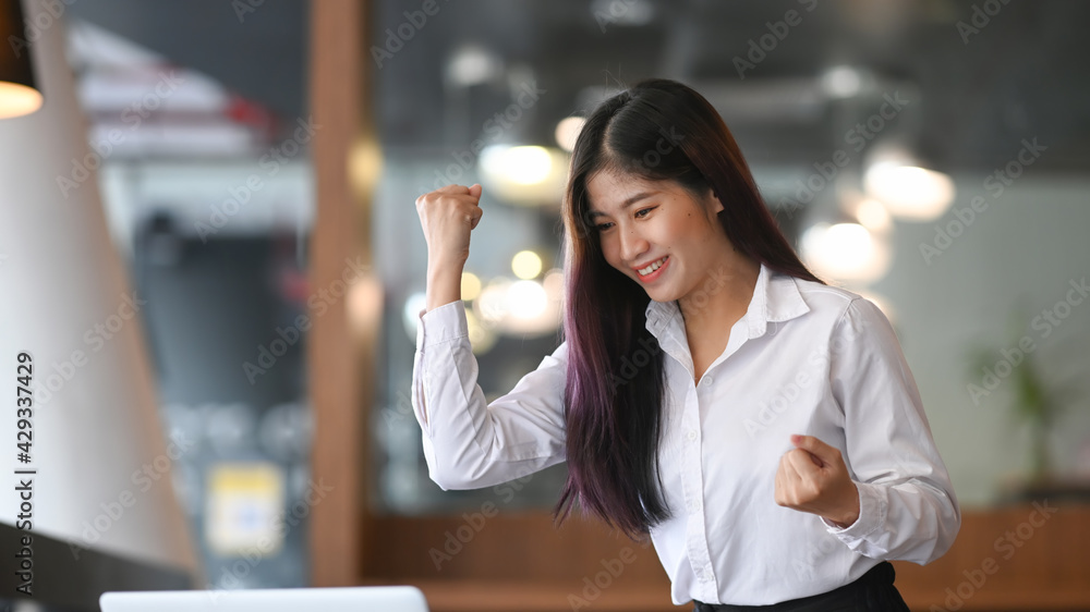 Excited businesswoman celebrating success achievement result while standing in front of her computer laptop at office.
