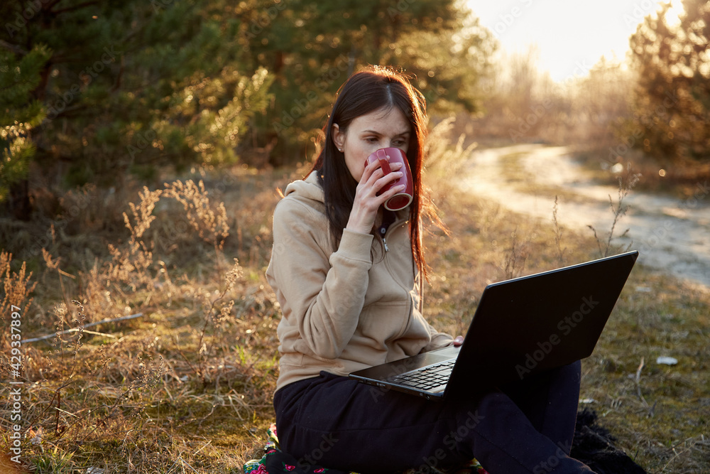 Young woman works with notebook and cup on nature. Loneliness (negative aspects of works on quarantine) and self-isolation concept Young woman works with notebook and cup on nature. Loneliness (negative aspects of works on quarantine) and self-isolation concept