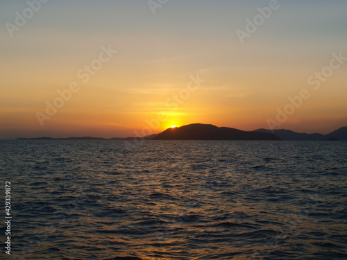 Sunset over the sea. Island on the horizon. Yellow orange glow on a clear sky. Ripple on the surface of the water. Waves  ocean  expanse of water. View from the sea  land in the distance. Andaman sea