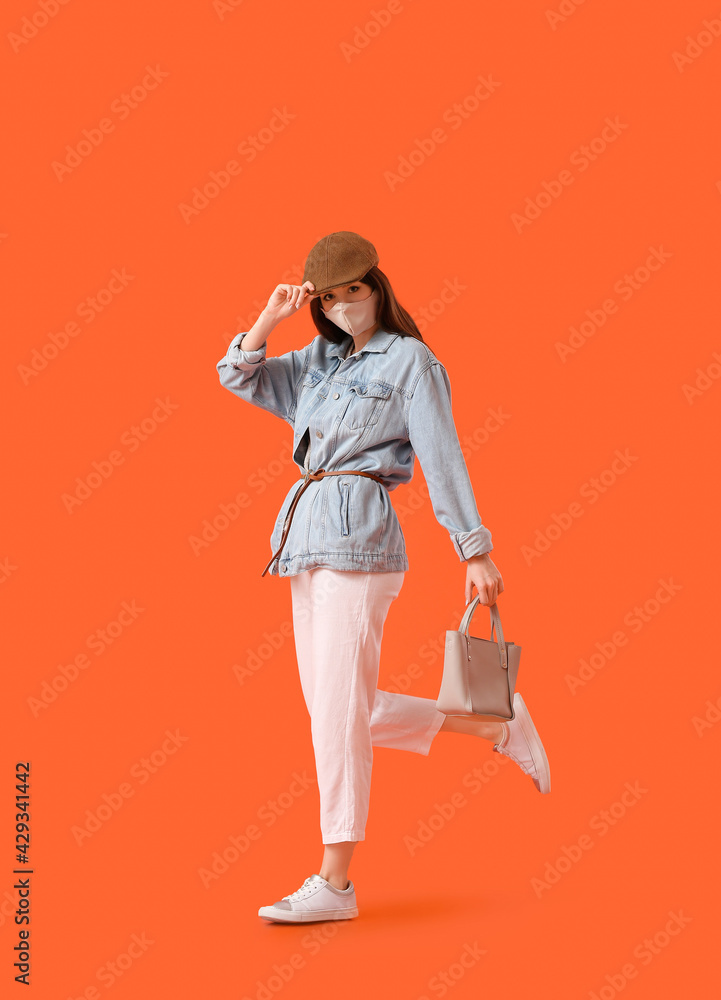 Fototapeta premium Fashionable young woman wearing mask on color background