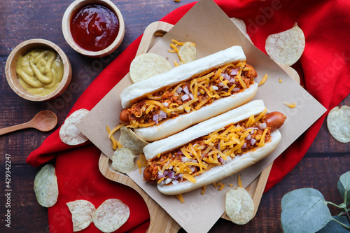 Chili dog, chili cheese hotdog served on wood tray of wood table with ketchup and mustard-  top view of American fast food