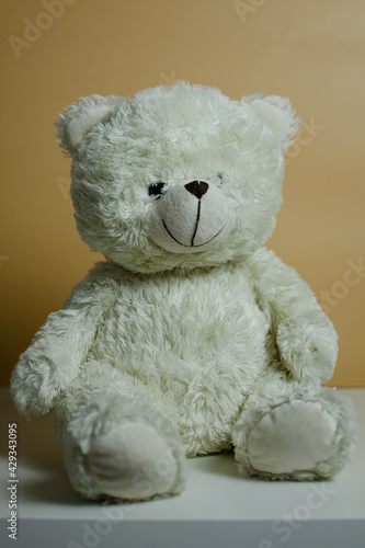 Toy polar bear sits on a plain beige background with artificial light