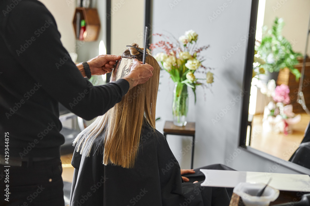 Naklejka premium Confident male stylist is dyeing hair of blond caucasian female client
