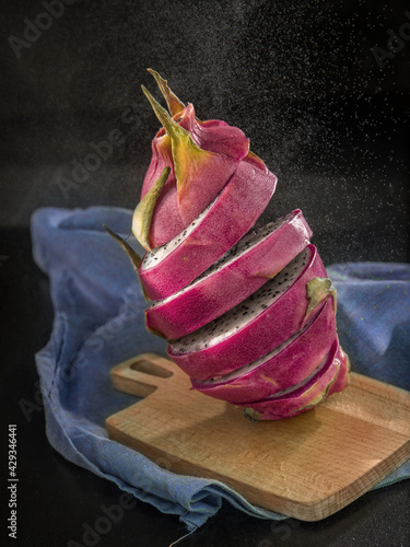 Sliced pink dradon fruit on a cutting board and black background .Balansed pieses of   pitahaya.   photo