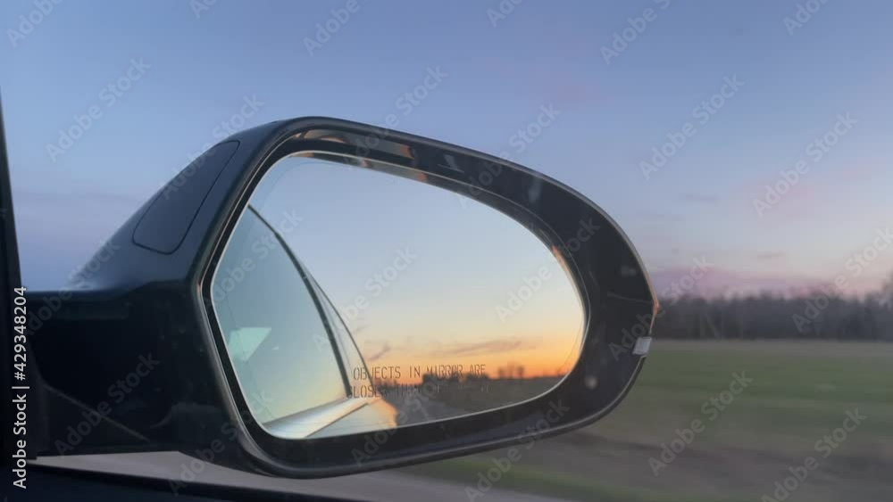 Reflection in Car Mirror while Driving during sunset on long empty road in rural area - late evening road trip looking out window into side sideview mirror on long rural drive Reflection in Car Mirror while Driving during sunset on long empty road in rural area - late evening road trip looking out window into side sideview mirror on long rural drive