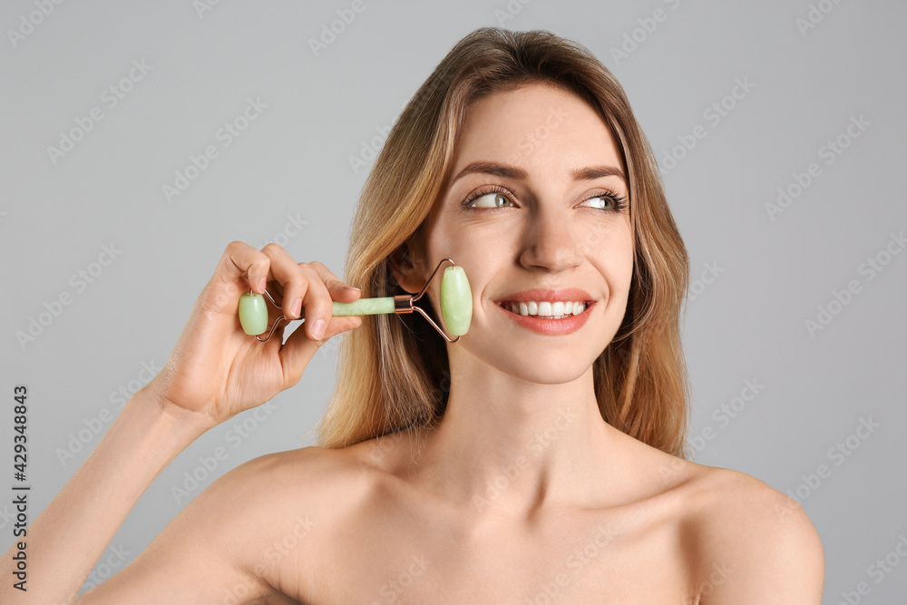 Young woman using natural jade face roller on light grey background Young woman using natural jade face roller on light grey background