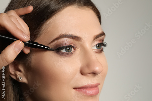 Artist applying black eyeliner onto woman's face on grey background, closeup