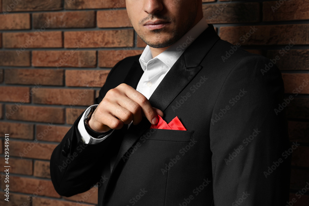 Man fixing handkerchief in breast pocket of his suit near brick wall,  closeup Stock Photo | Adobe Stock