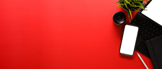 Overhead shot of bright red desk with office supplies and mock up smartphone