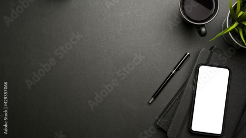 Top view of dark creative workspace with smartphone, stationery, mug and copy space