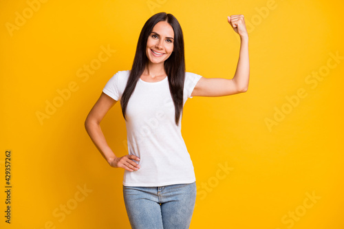 Photo portrait of brunette girl in stylish clothes showing strength triceps smiling isolated on vivid yellow color background