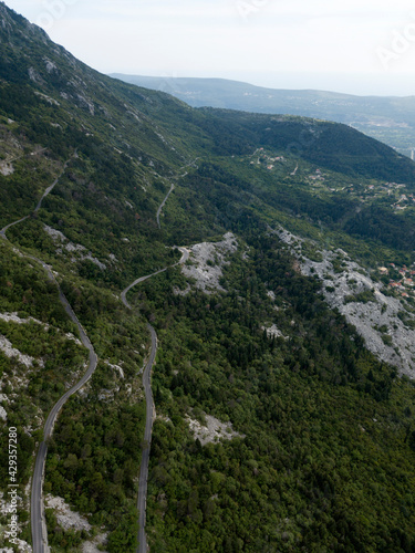 Aerial top down view of forest winding road in mountains, Montenegro. Long curving road on hills, rich vegetation, Mediterranean bush. Mountain ranges on the horizon. Summer. Travel on nature