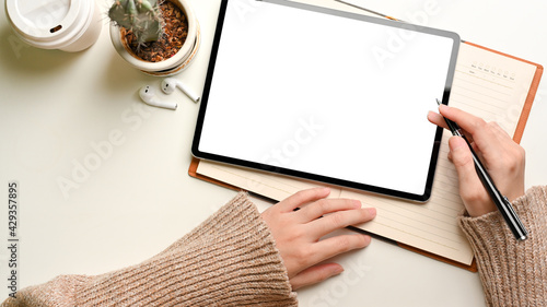 Top view of female working with digital tablet and notebook on white table