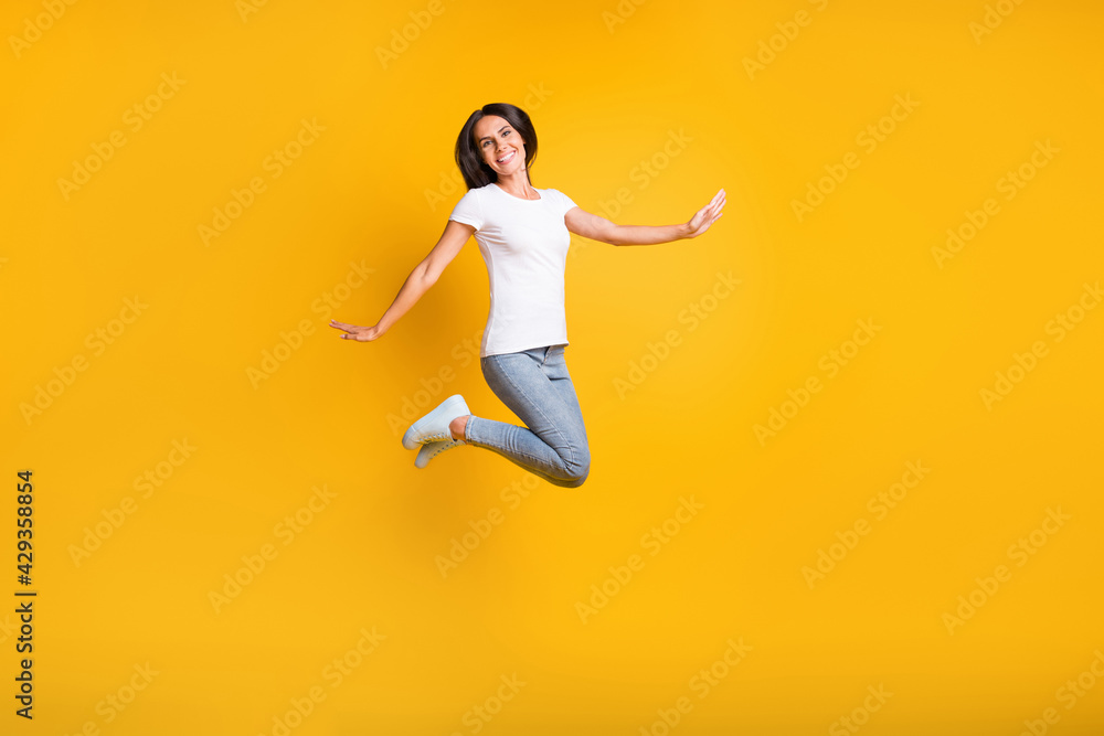 Full length photo of charming pretty young woman jump ups air raise hands isolated on shine yellow color background