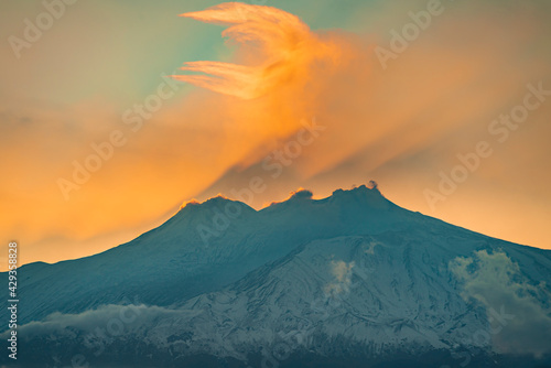 Hazy silhouette of Mount Etna and its shadow by the orange sunset light 
