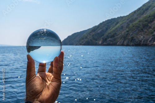 Crystal ball in the man’s hand. Original upside down view and rounded perspective of the sky and sea. photo