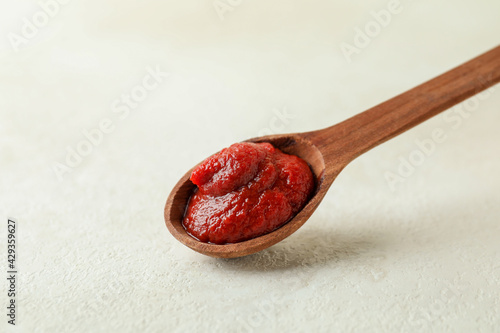 Wooden spoon with tomato paste on white textured background