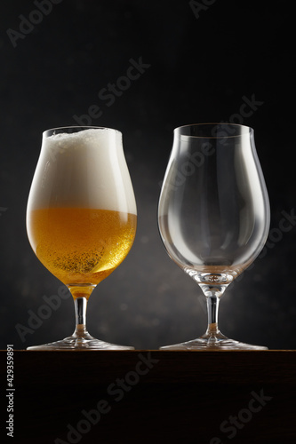 Glass with light golden beer and empty glass on a dark background