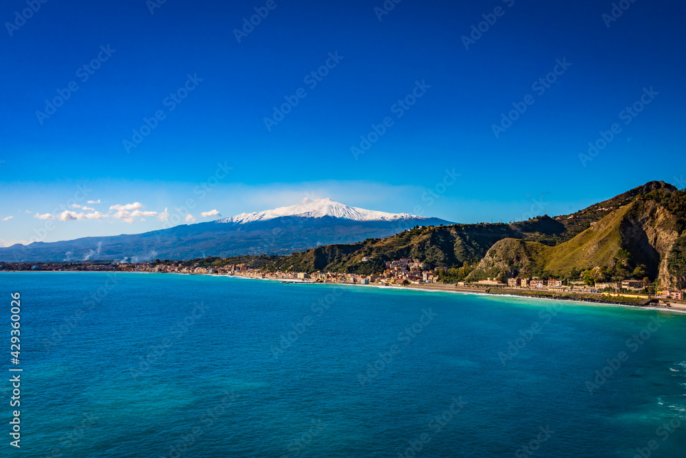 Blue sea on the coast of Giardini Naxos, Mount Etna covered by snow in the background 